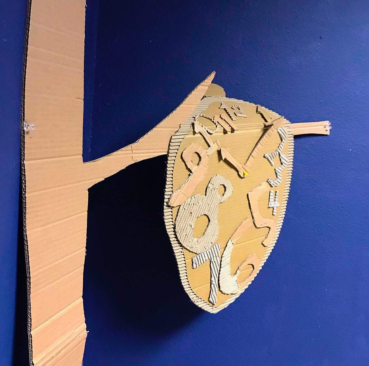 Cardboard clock art hanging from cardboard branch